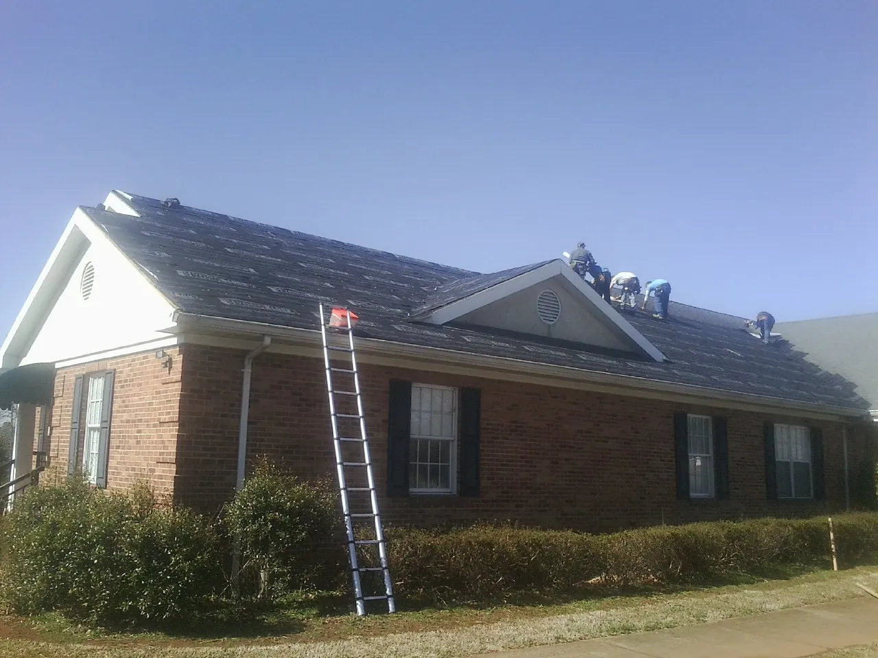 Crew tearing shingles off a brick ranch roof with a ladder set — Emergency Roof Repair work by our crew in Chino Hills