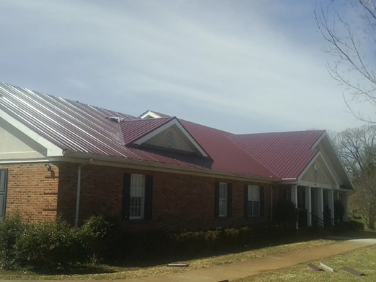 Red metal roof with gabled entries on a long brick building, from a Hail Damage Roof Repair job in Chino Hills