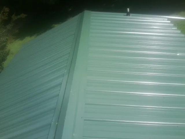 New green metal panels meeting at the ridge of a roof — Flat Roof Repair work by our crew in Chino Hills