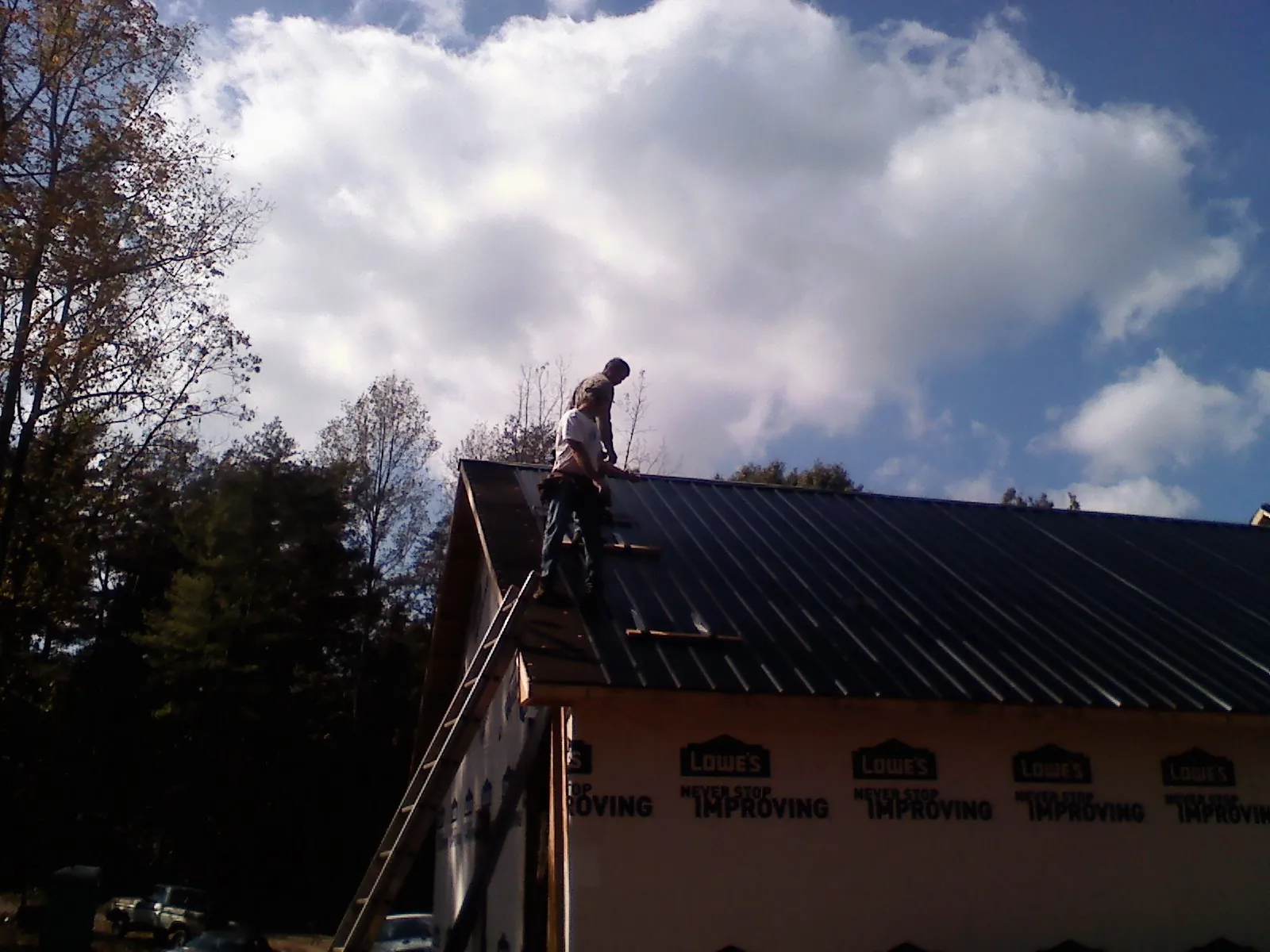 Roofer fastening dark metal panels high against a cloudy sky, from a Roof Inspection job in Chino Hills