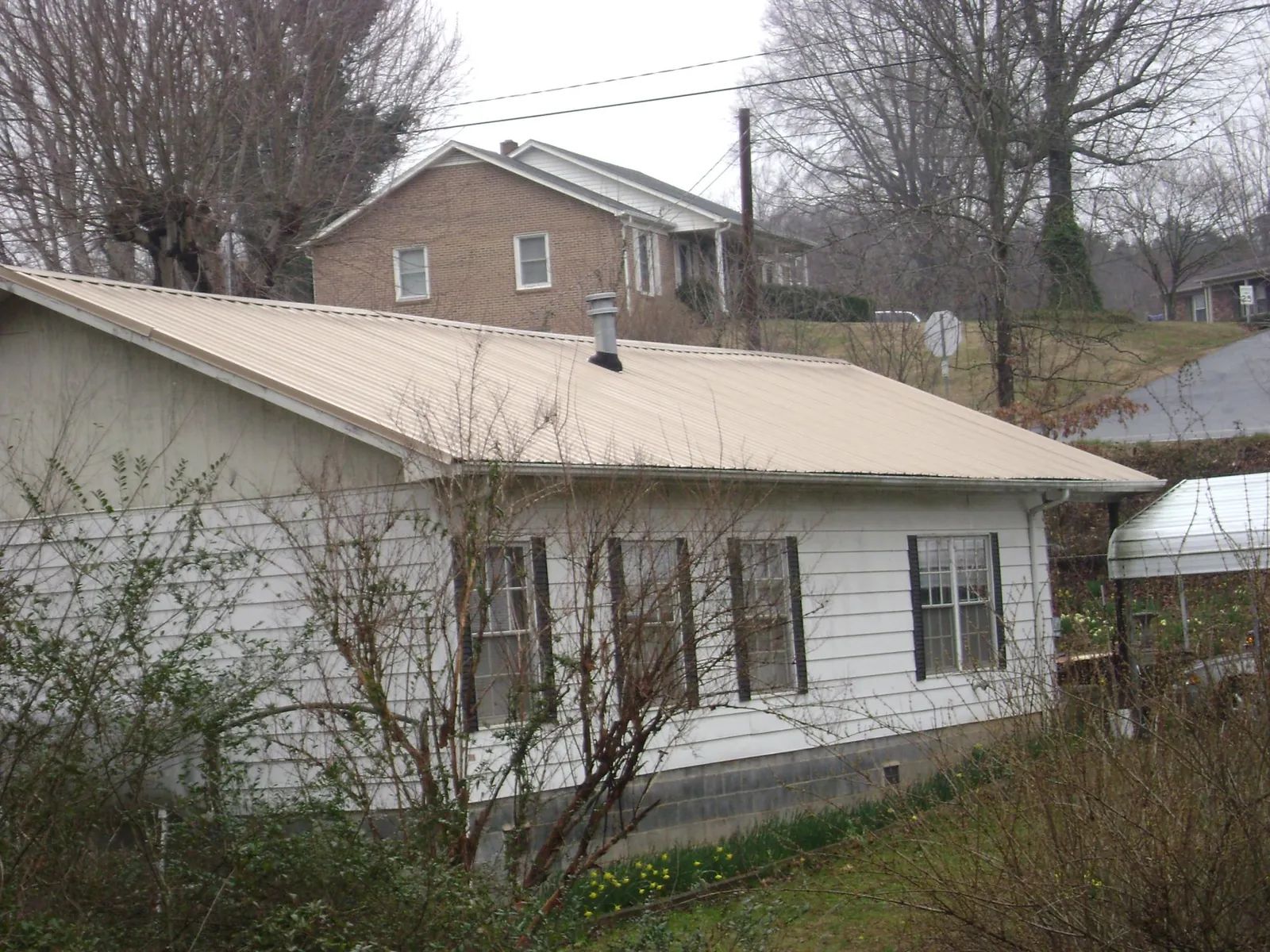 Tan metal roof on a white sided house set into a hillside — Commercial Roofing by Roofing Brothers in Chino Hills
